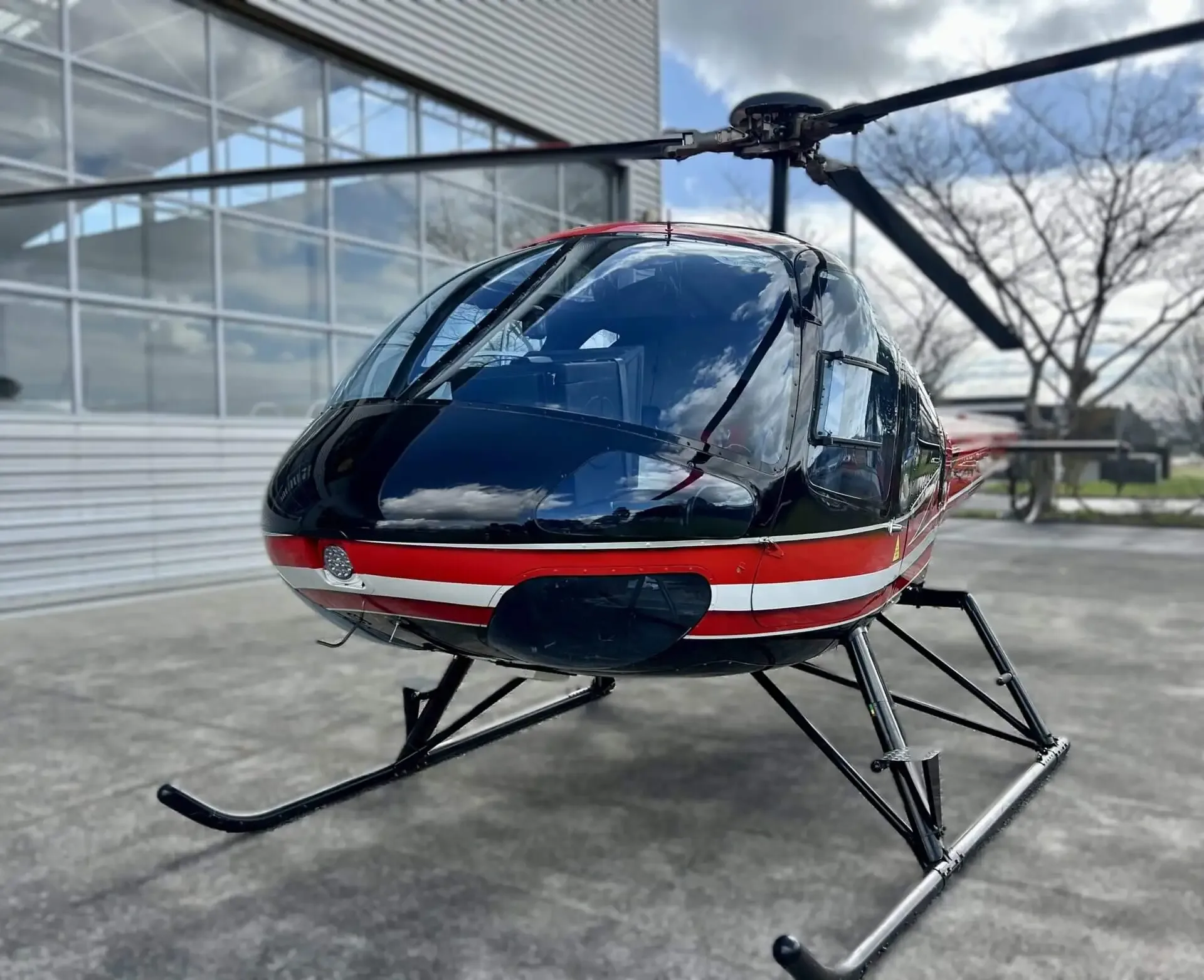 A close-up front view of a red and black helicopter with a large clear bubble canopy, parked outdoors.