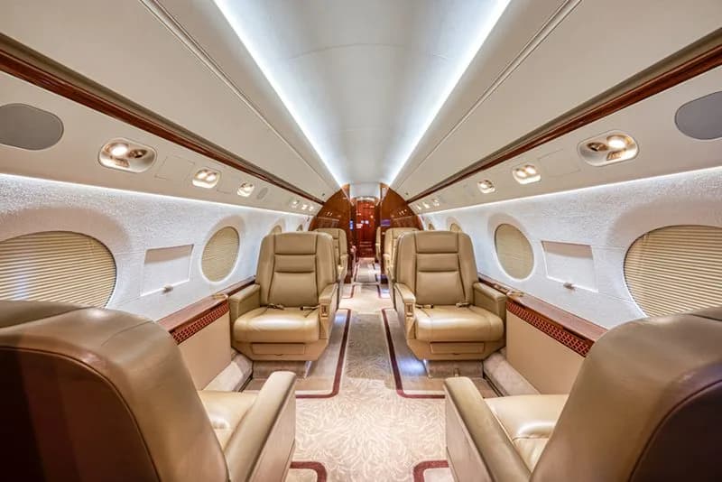 The luxurious cabin interior of a business jet with tan leather seats and a patterned aisle carpet.