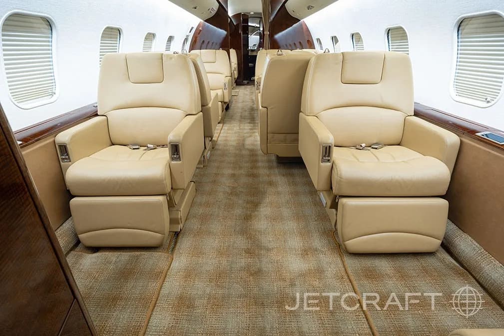 A wide view of the aircraft cabin featuring rows of beige leather seats and patterned carpet.