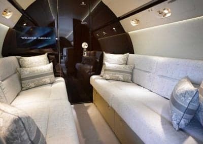 Aircraft interior featuring cream-colored sofas and a TV screen.