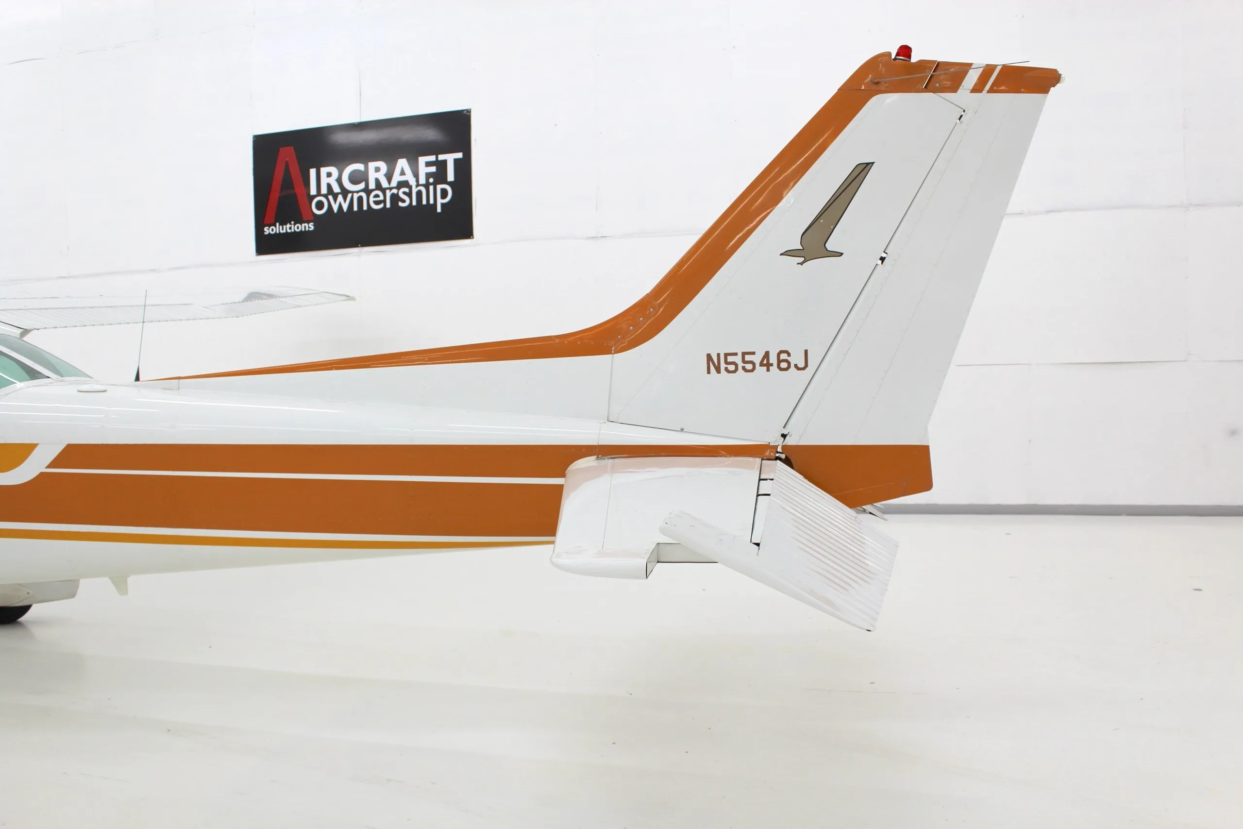 A close-up view of the white and orange tail section of a Cessna Skyhawk II (N5546J) in a hangar.