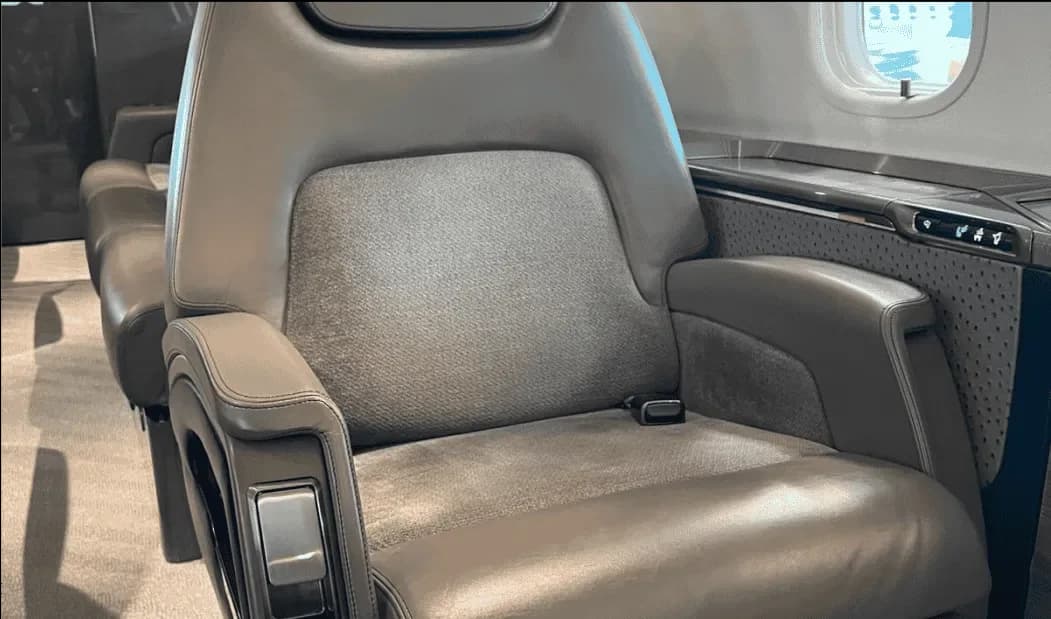 A close-up view of a grey leather aircraft cabin seat with a textured fabric insert.