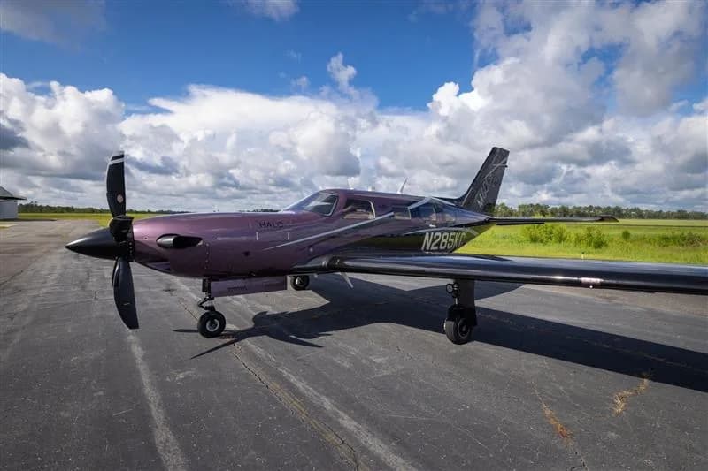 A Piper M500 aircraft is parked on the tarmac with a field in the background.