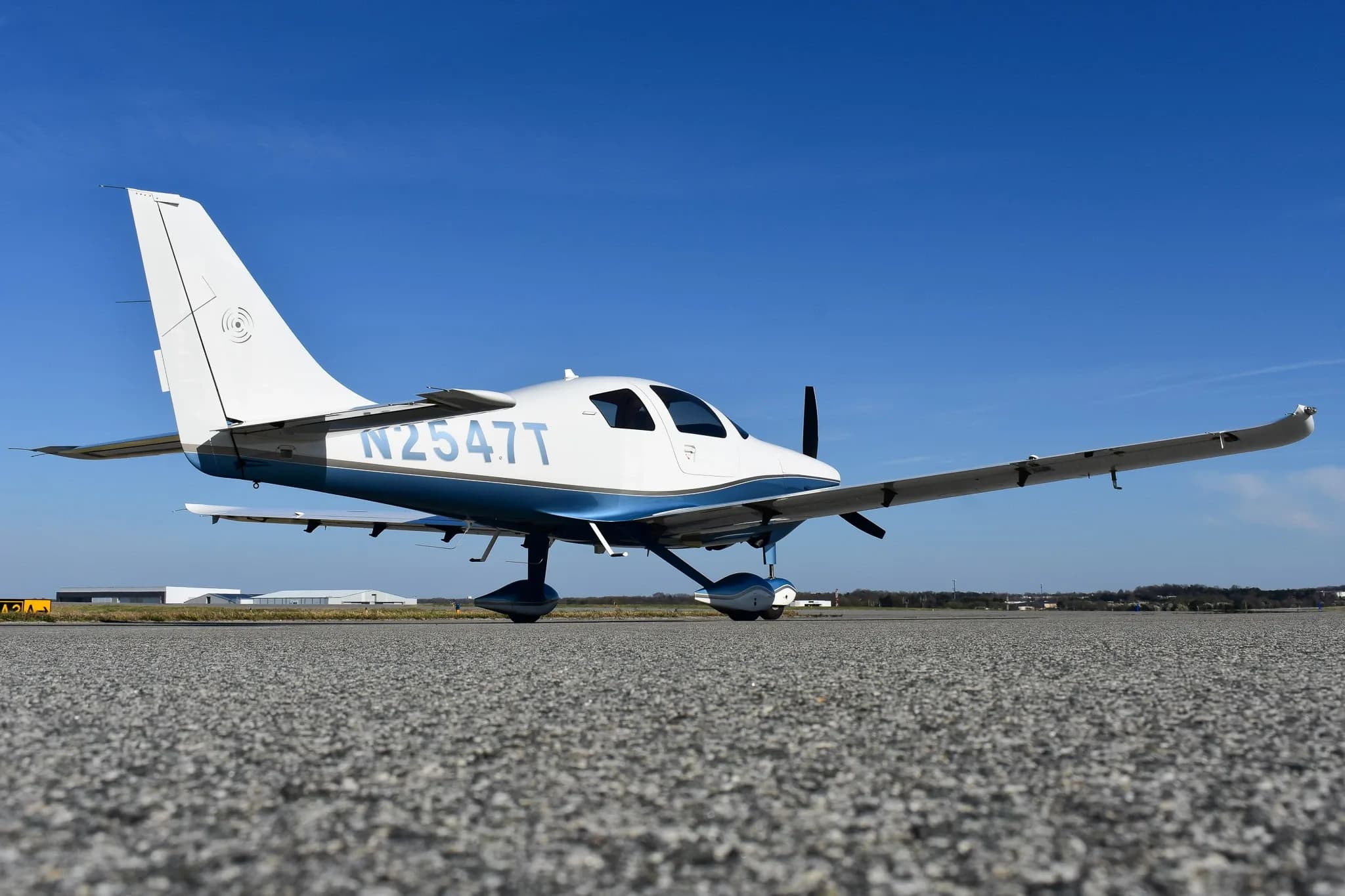 A low-angle side view of the white and blue single-engine aircraft, N2547T, parked on an asphalt runway.