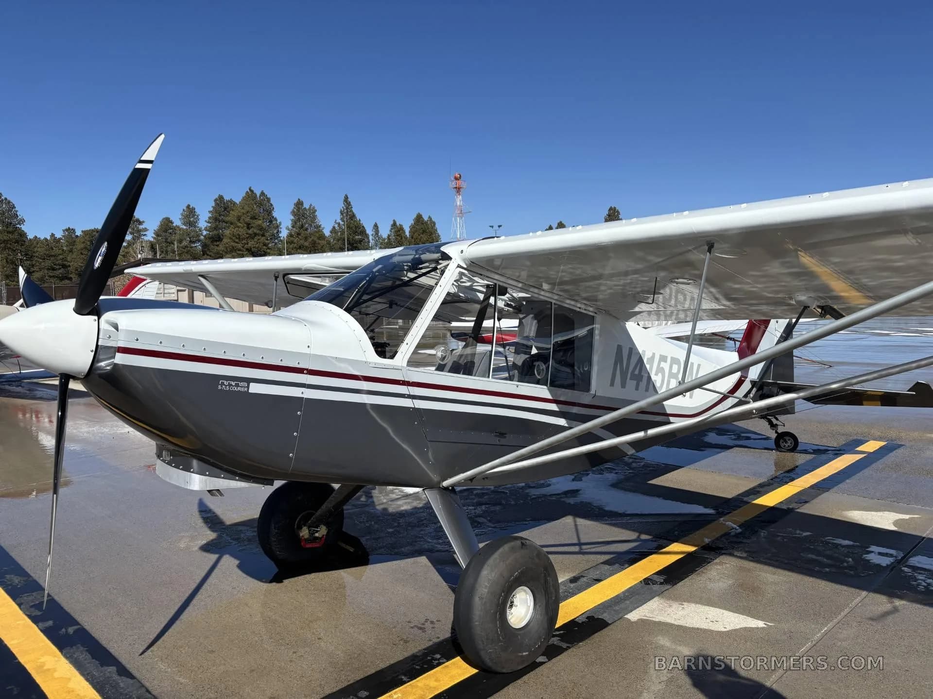 A white and grey Rans S-21 Outbound aircraft, N415BW, parked on a tarmac with a propeller in the foreground.