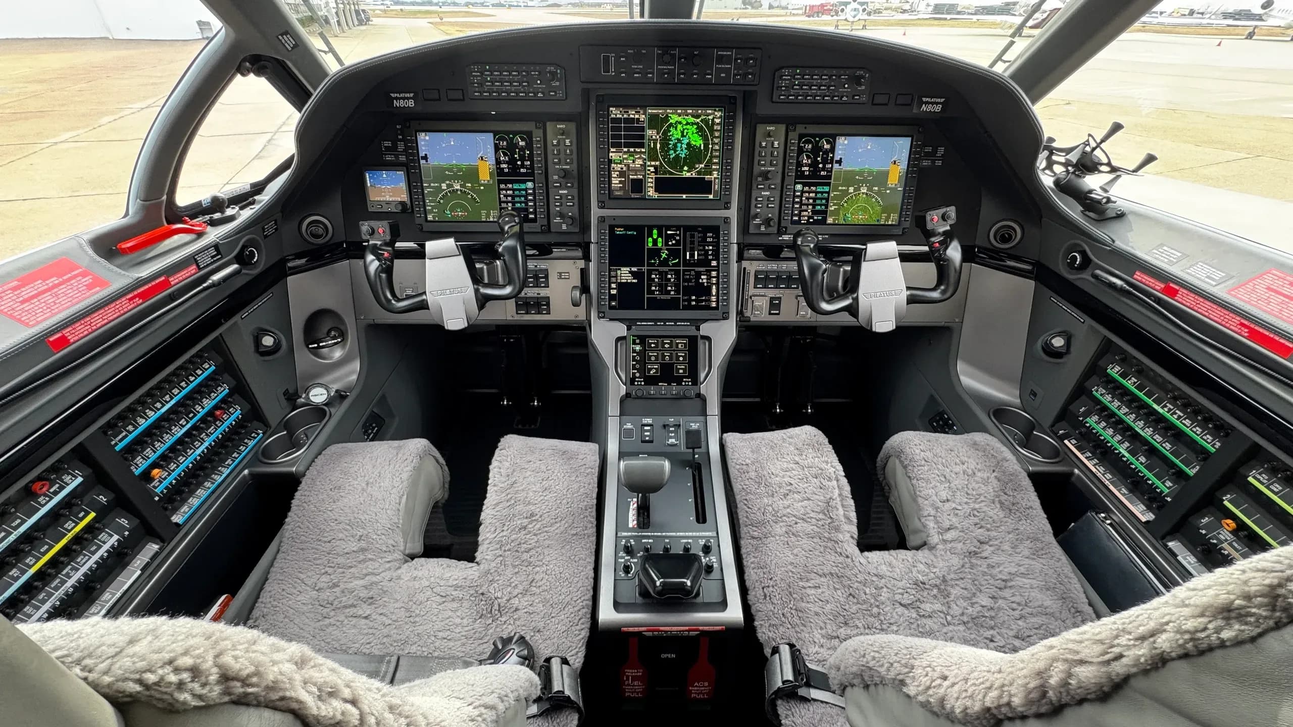 The luxurious light grey interior cabin of a Pilatus PC-12, with quilted leather seats and overhead lighting.