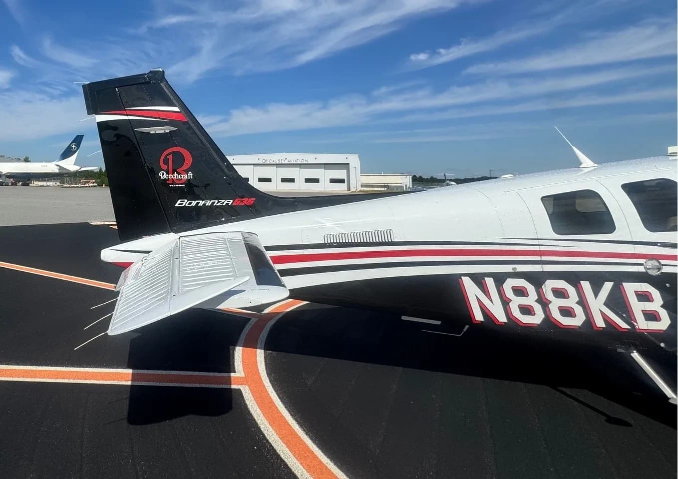A rear three-quarter view of the white and black Beechcraft Bonanza, tail number N88KB, on an airport tarmac.