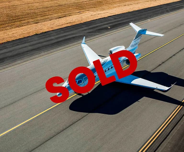 An aerial view of a blue and white Gulfstream G280 business jet on an asphalt runway.