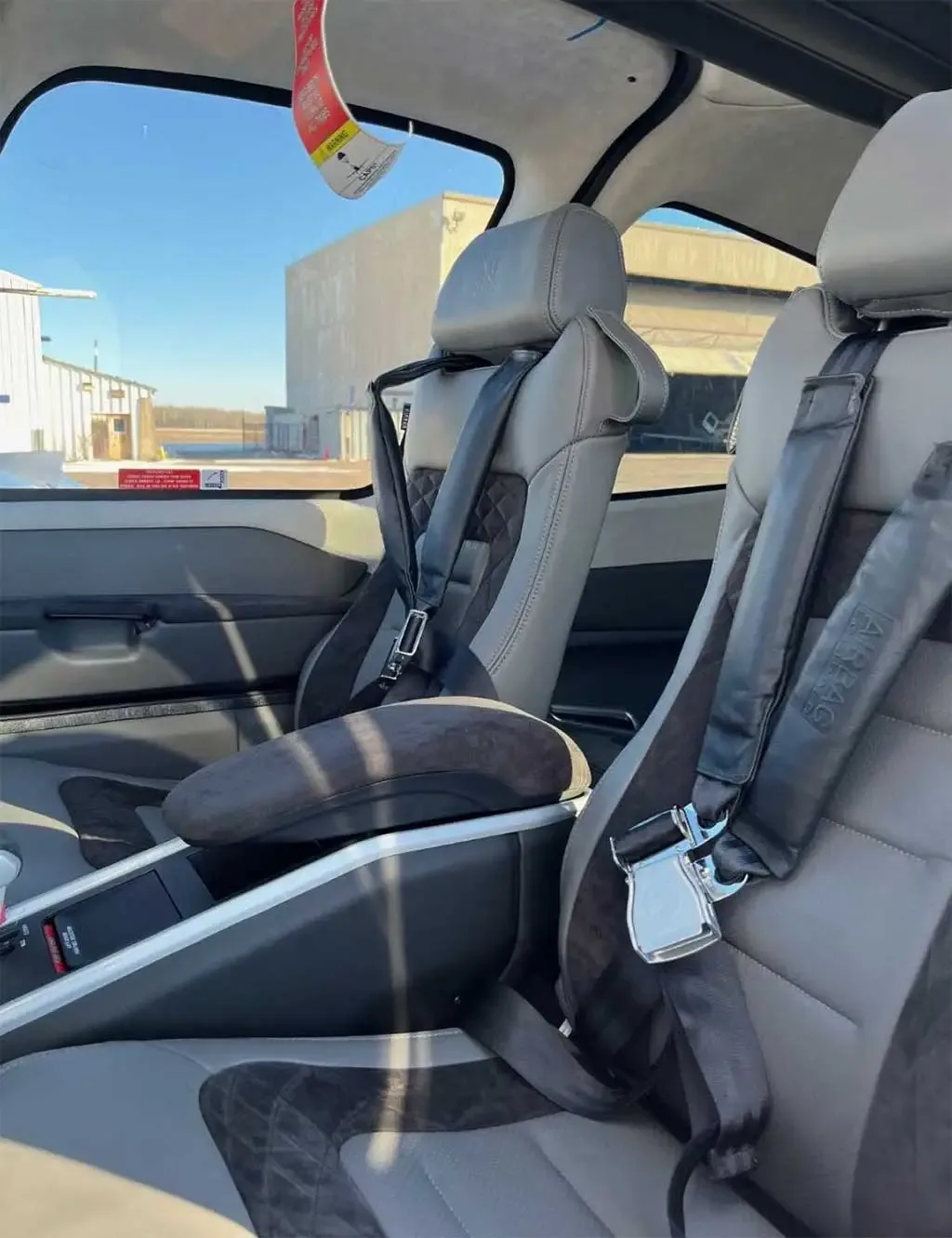 The grey and black leather interior of a Cirrus aircraft cabin, showing two front seats with seatbelts.