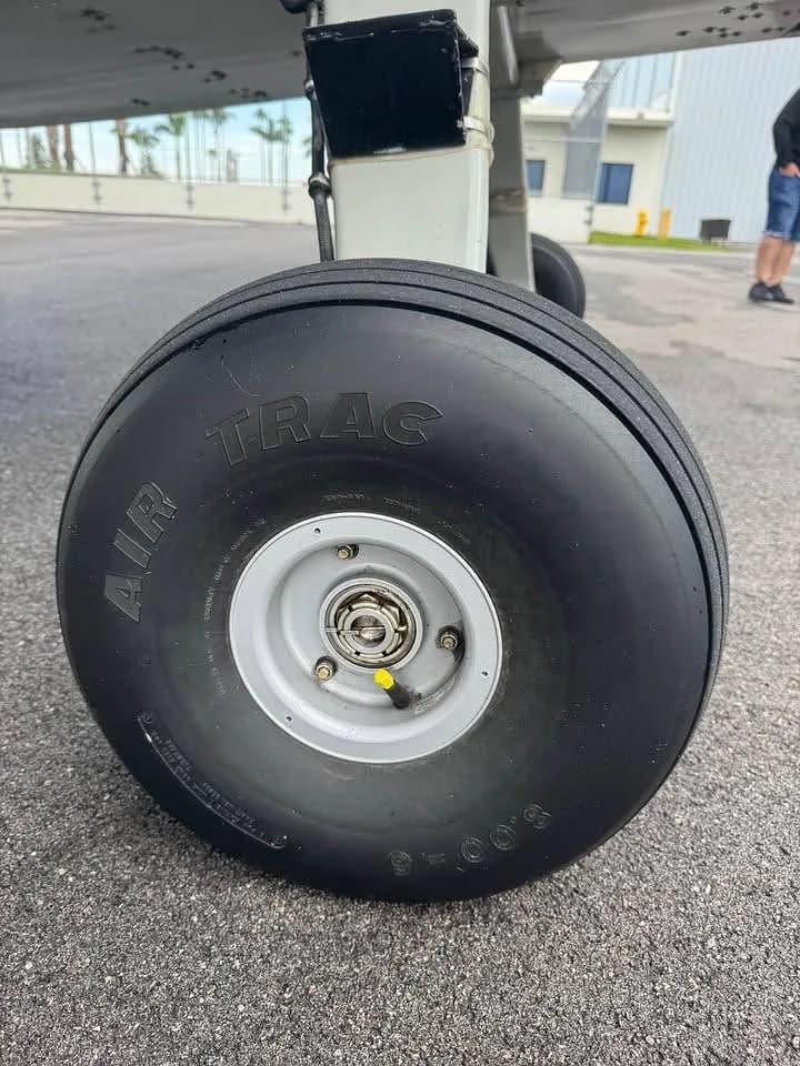 A close-up view of the main landing gear wheel with an "AIR TRAC" tire on a tarmac.
