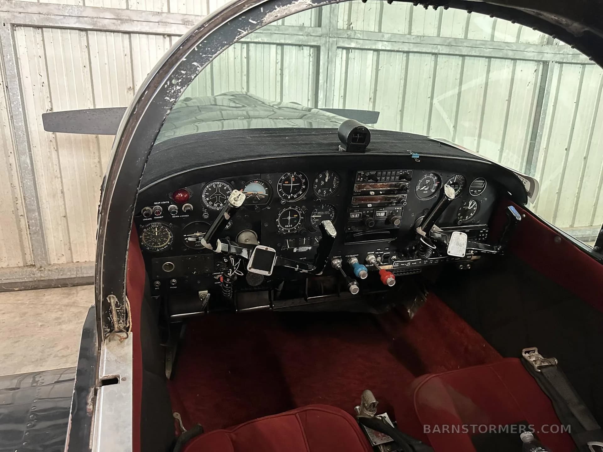 The cockpit of a black aircraft, showing the instrument panel with various gauges and switches, and red seats.