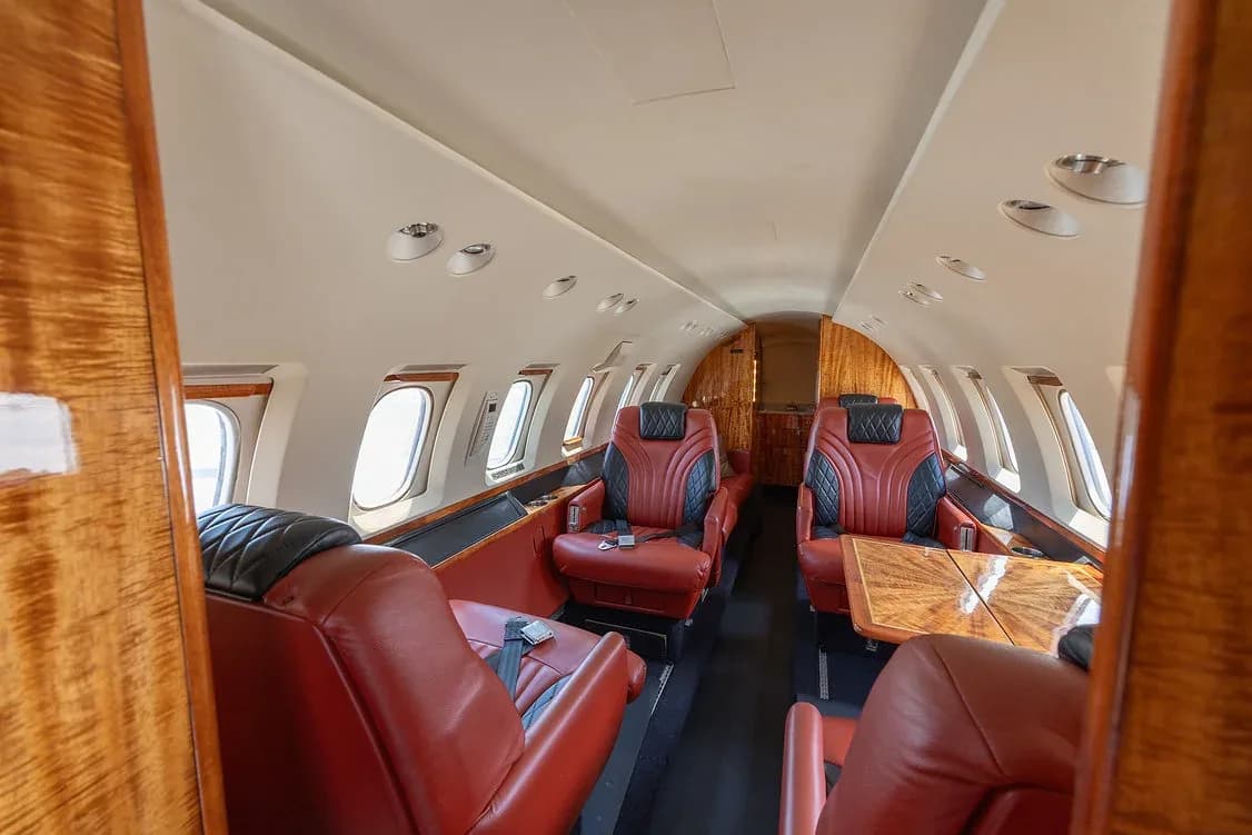 The luxurious interior cabin of a private jet, featuring red and black leather seats and polished wood paneling.
