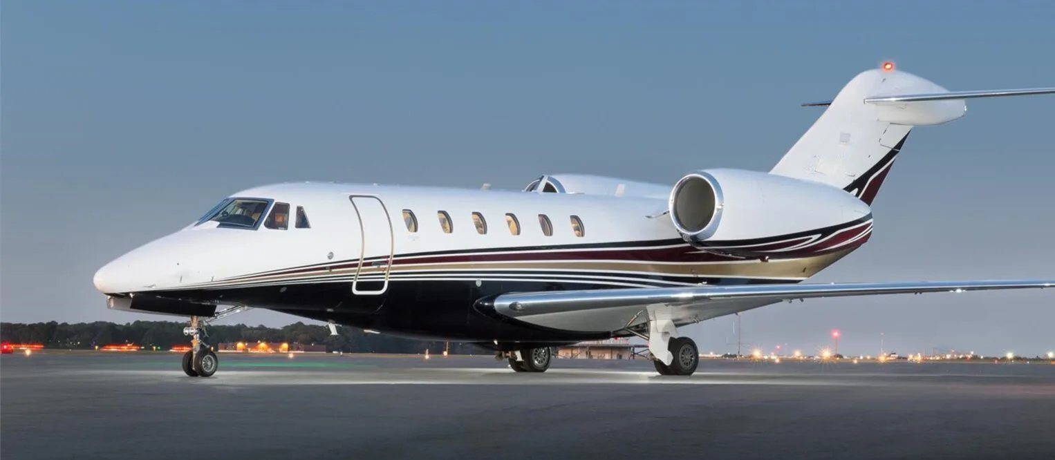 Side view of a white and maroon Cessna Citation on the tarmac at dusk.