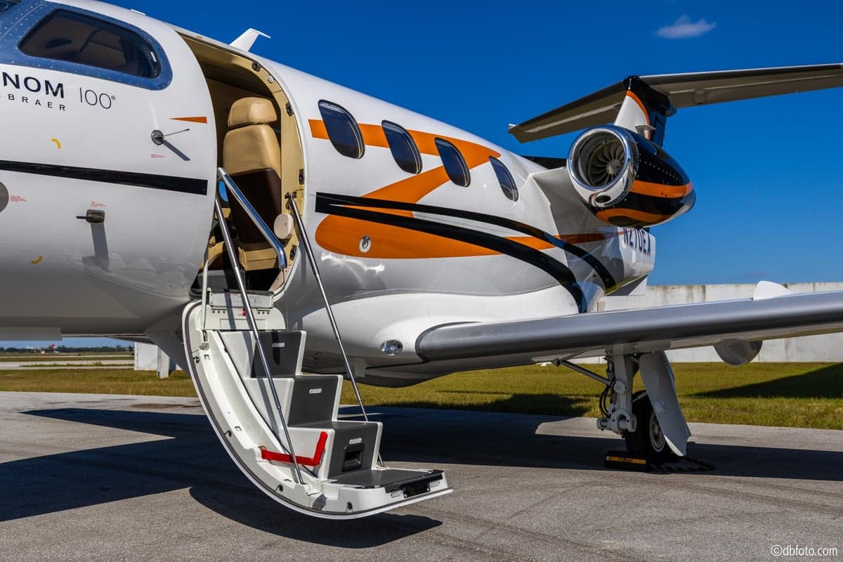 A Phenom 100 aircraft with the door open and stairs extended.
