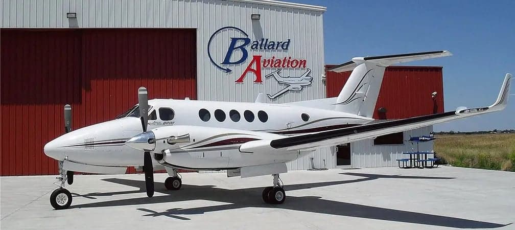 A King Air B200 is parked in front of the Ballard Aviation hangar.