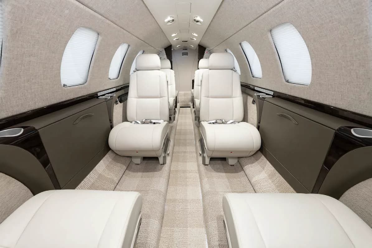 The luxurious cabin interior of a private jet, featuring light-colored leather seats and a patterned carpet.