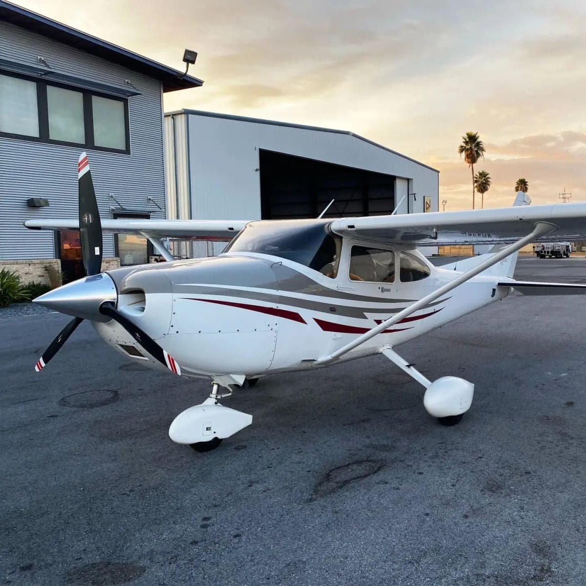 A Cessna 172 Skyhawk parked in front of a hangar at sunset.