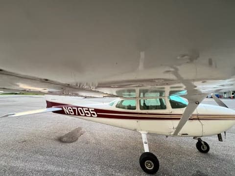 A side view of the white Cessna 172, N97055, with maroon and gold stripes, parked on an asphalt surface.