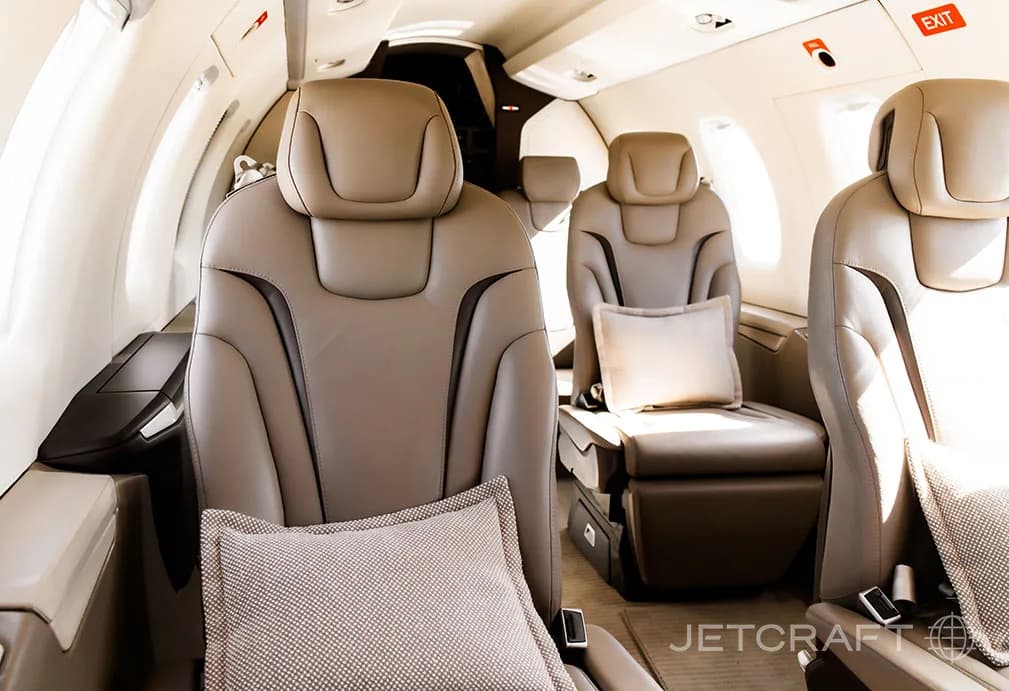 A close-up view of the light brown leather seats in the aircraft cabin, with a small pillow on one seat.
