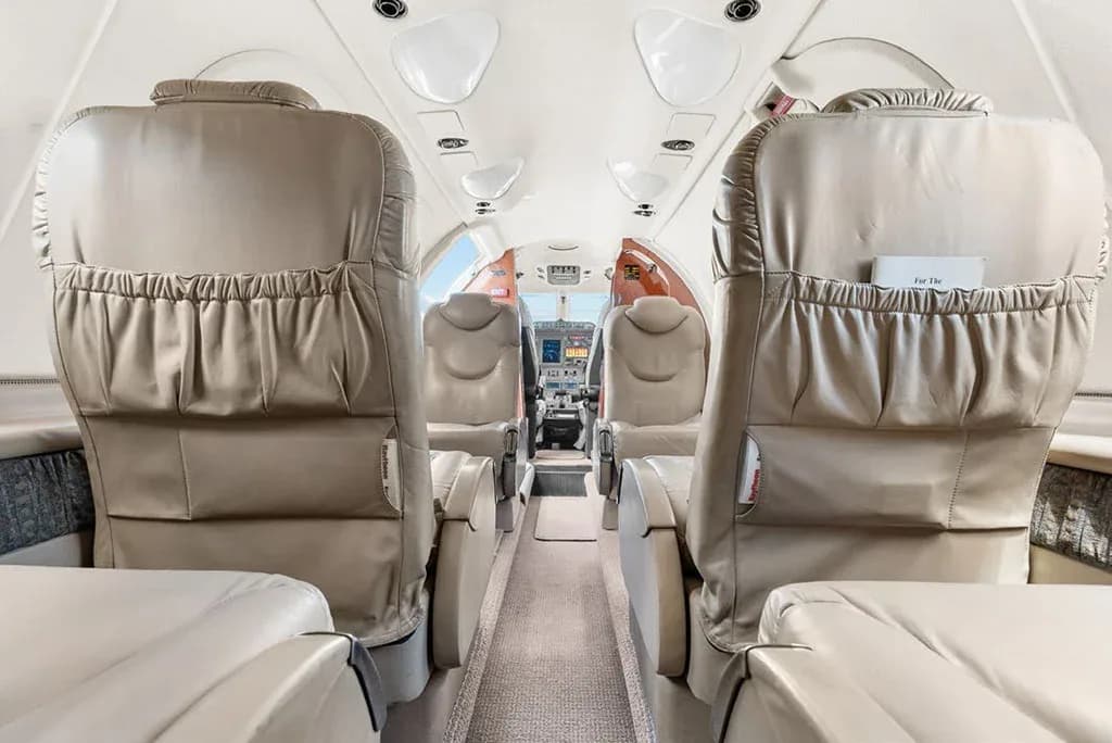 A long view down the private jet's cabin aisle, showing multiple rows of beige leather seats leading to the cockpit.