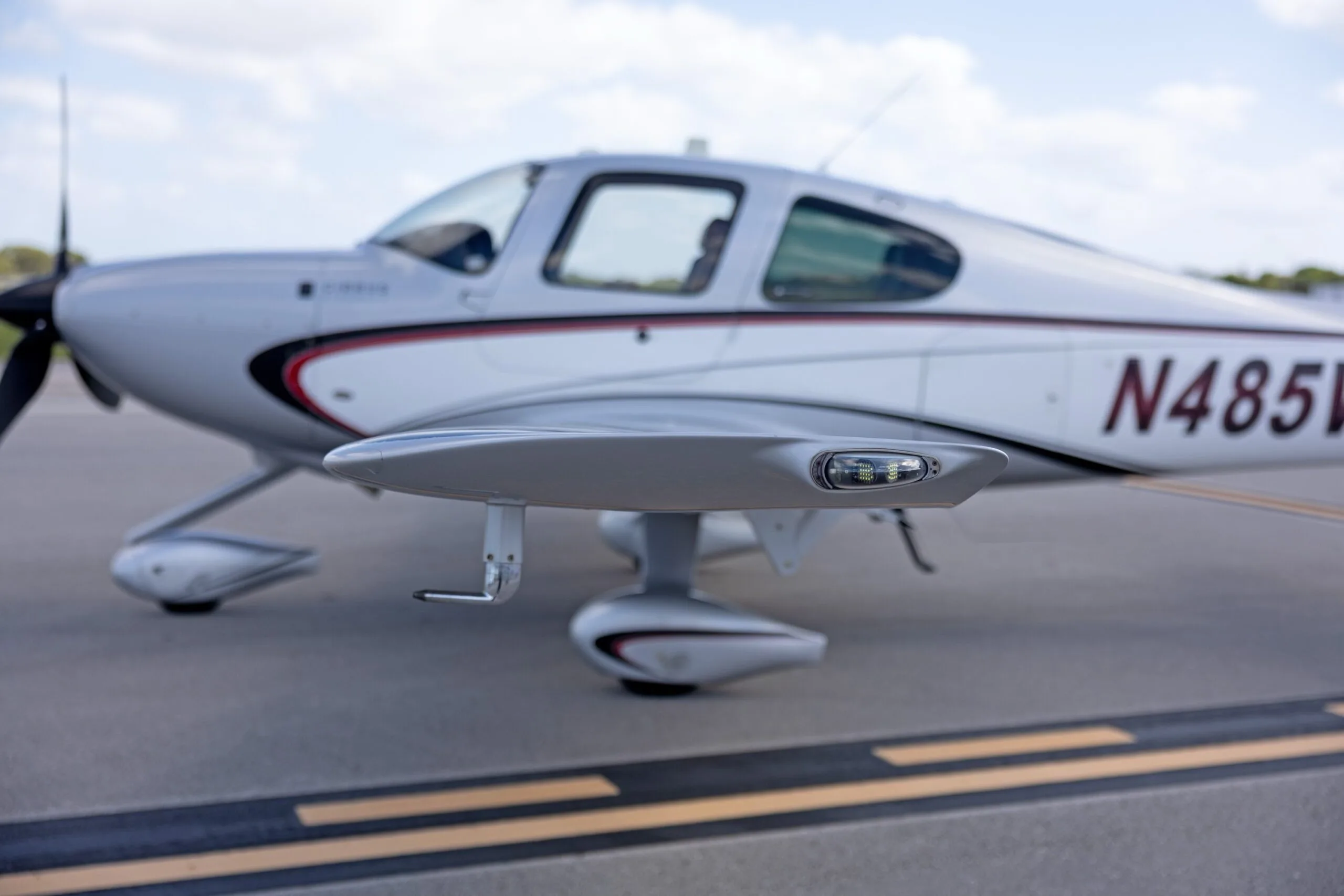 A close-up, blurred side view of the silver Cirrus SR22 GTS aircraft N485VB, focusing on the wingtip and landing gear.