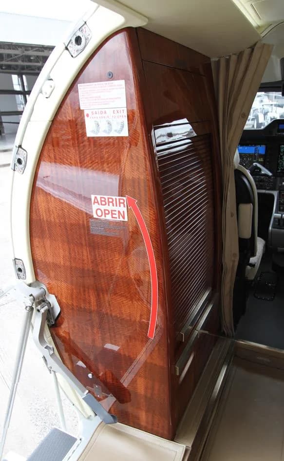 The Phenom 300E cabin features a wooden door with an emergency exit sign.