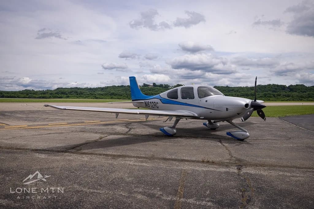 A silver and blue Cirrus SR22T Carbon aircraft, registration N612RC, parked on an airfield under a cloudy sky.