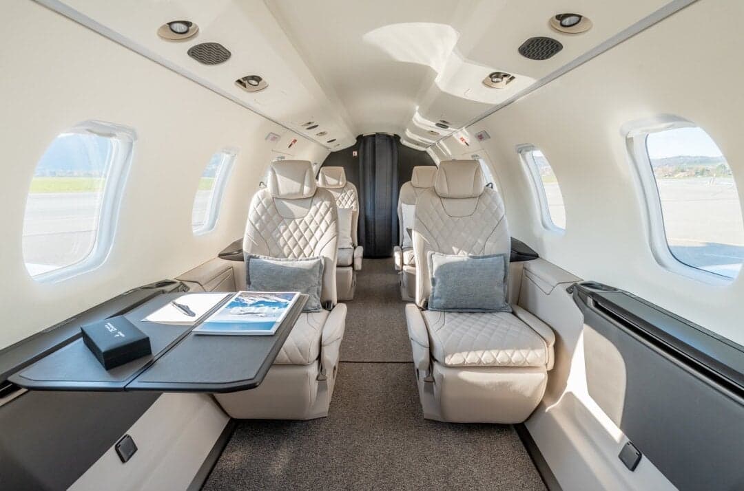 The luxurious interior of a private jet cabin with light-colored quilted leather seats and pull-out tables.