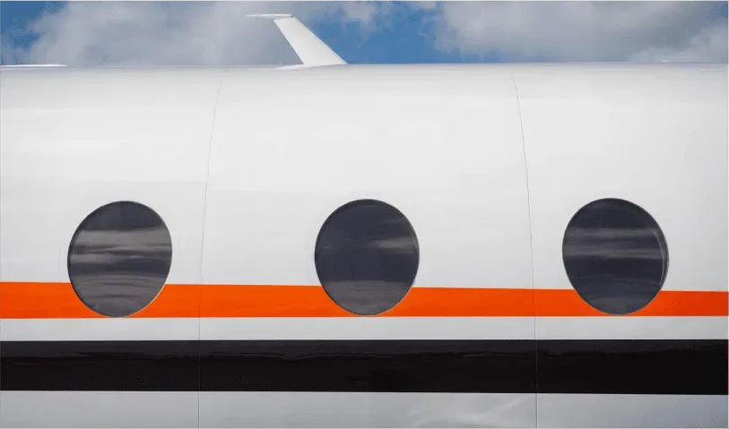 Close-up of the white aircraft fuselage showing three oval windows and orange and black stripes.