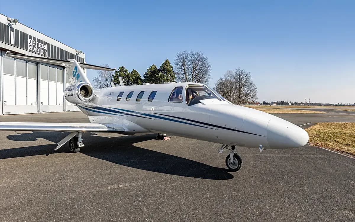 A white business jet with blue stripes is parked on a tarmac next to a 'general aviation' hangar under a clear blue sky.