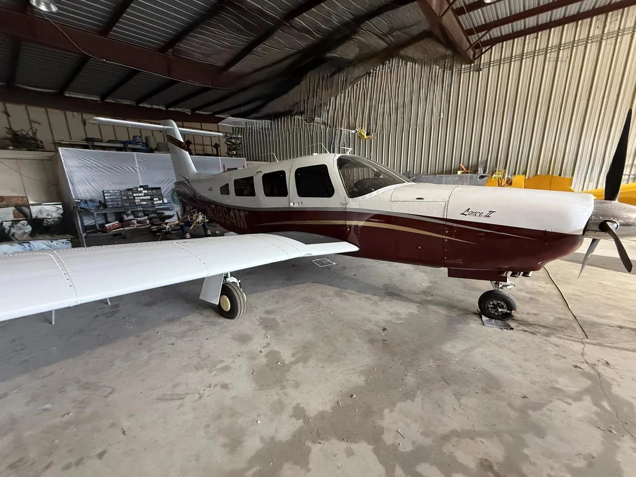 A Piper Lance II aircraft with a white and maroon paint scheme, parked inside a hangar.