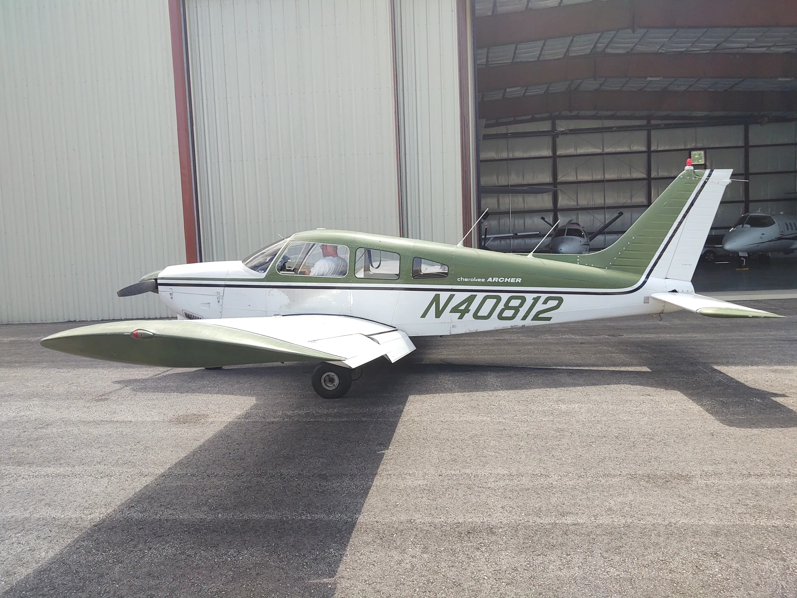 A white and green Piper Cherokee Archer aircraft with registration N40812 parked on an asphalt ramp outside a hangar.