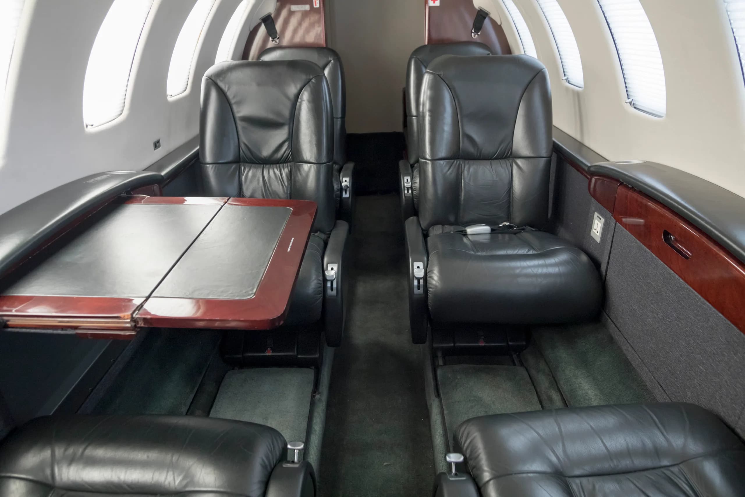 The interior cabin of a private jet with black leather seats facing each other and a fold-out table.