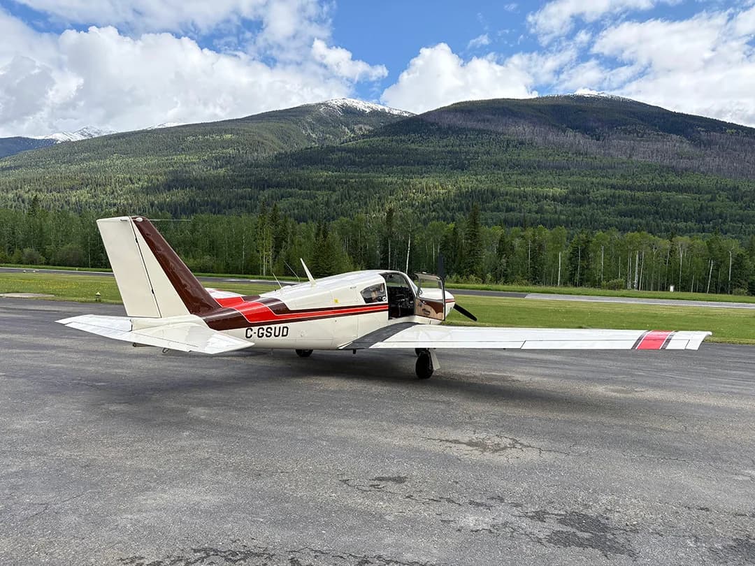 Side view of a white and brown aircraft with the registration C-GSUD parked on an airport tarmac with its door open.