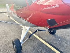 Close-up of the landing gear of the red and silver Carbon Cub N7XU.