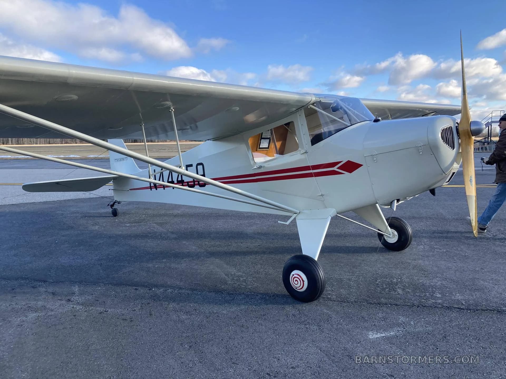 A three-quarter front view of a white and red Piper Cub N44459 with a wooden propeller, parked on an airfield.