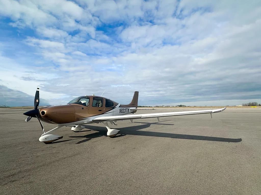 A Cirrus SR22 aircraft, N823TK, with a brown and white paint scheme parked on an airfield.