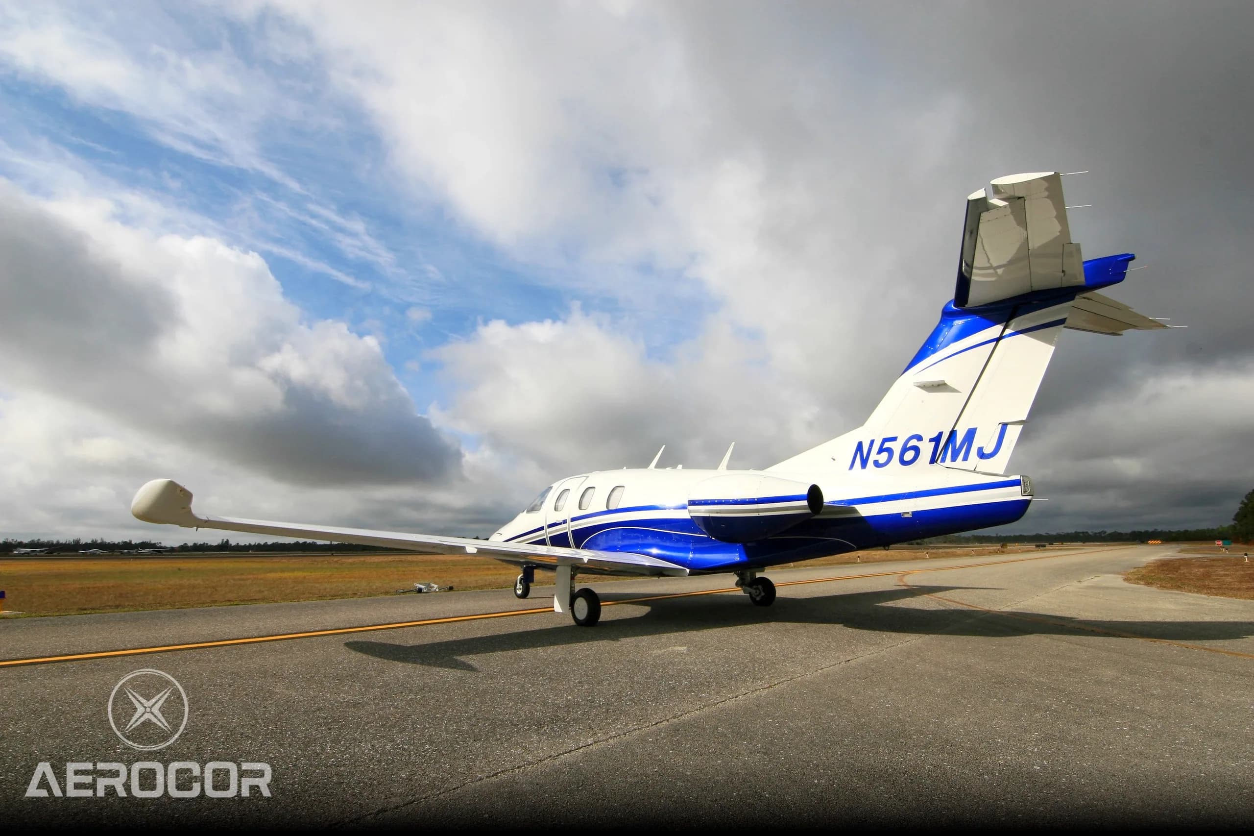 Rear three-quarter view of a white and blue Eclipse 500 jet, registration N561MJ, on an airfield.