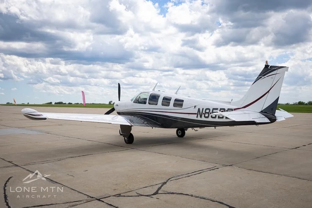 A white and dark grey Beechcraft Baron N85BB parked on a tarmac under a partly cloudy sky.