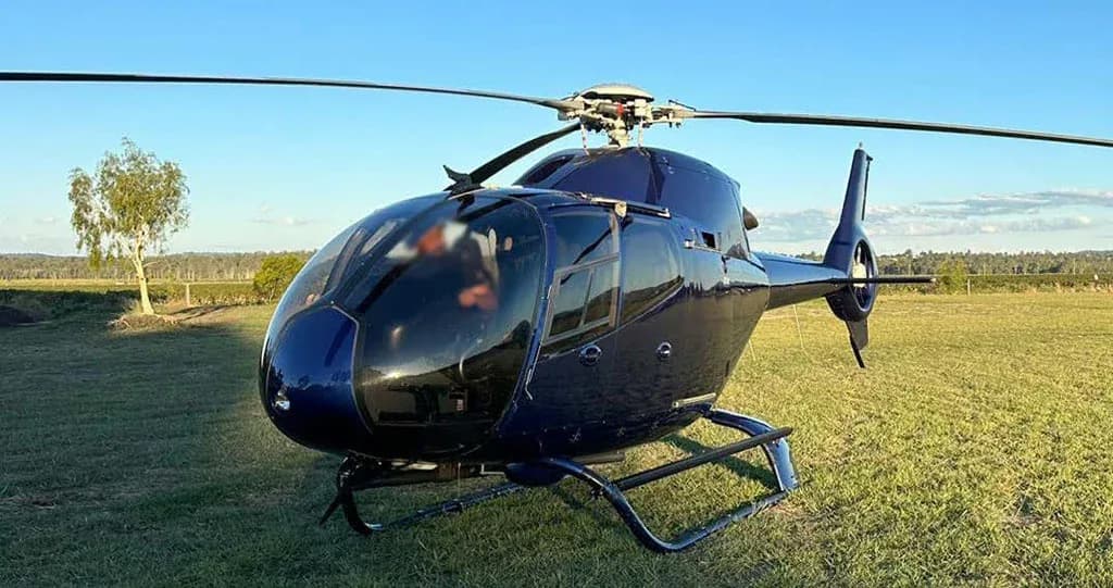 A dark blue helicopter with a large bubble canopy is parked on a green grassy field.