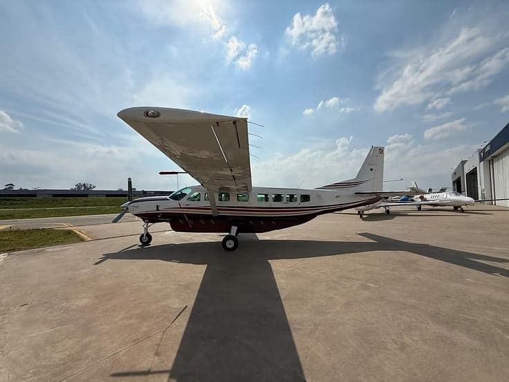 A maroon and white Cessna Caravan parked on the tarmac with other aircraft nearby.