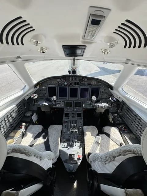 The cockpit of a business jet, featuring multiple display screens and control panels.