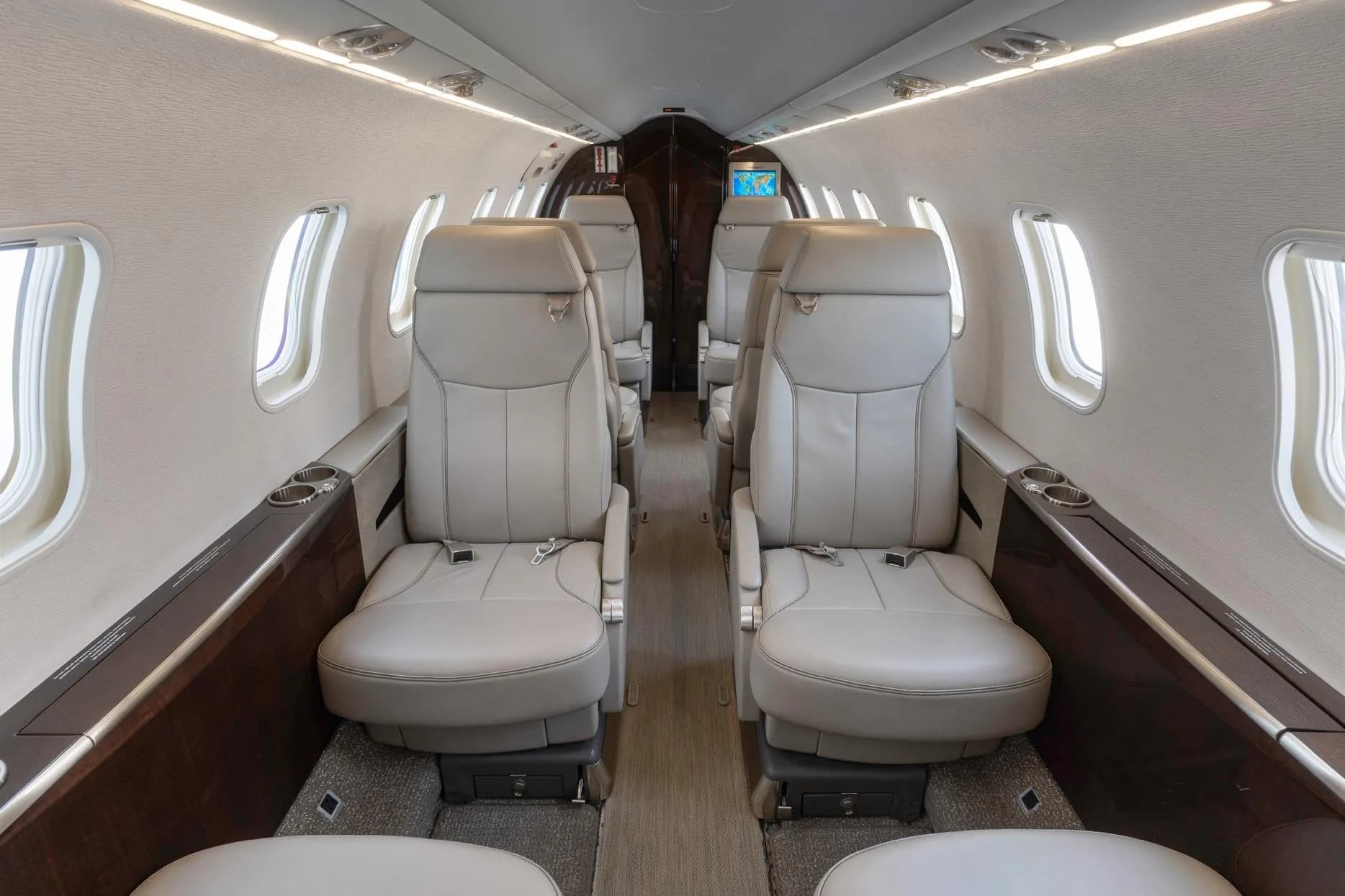 View down the aisle of a private jet cabin with light gray leather seats and dark wood accents.