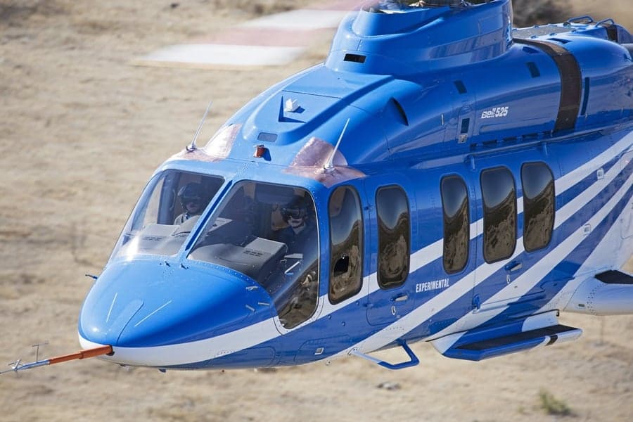 Close-up of the nose of a blue Bell 525 helicopter with pilots visible in the cockpit.