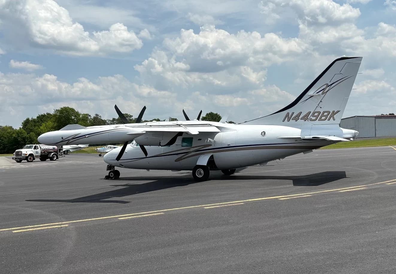 Side view of a white twin-engine aircraft with registration N449BK and blue and gold stripes on an airfield.