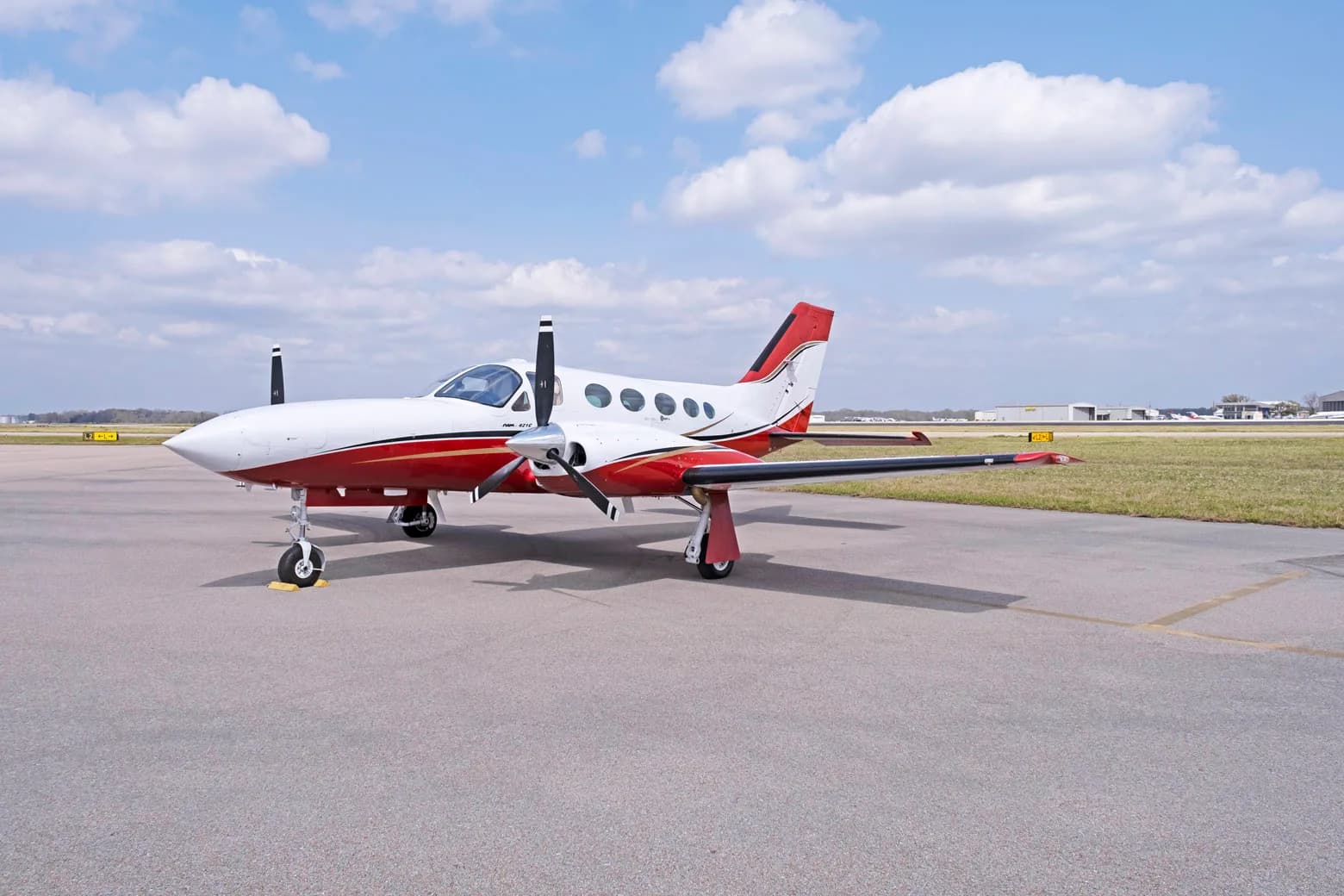 A white and red twin-engine propeller aircraft, a Cessna 421C Golden Eagle, parked on an asphalt tarmac under a partly cloudy sky.