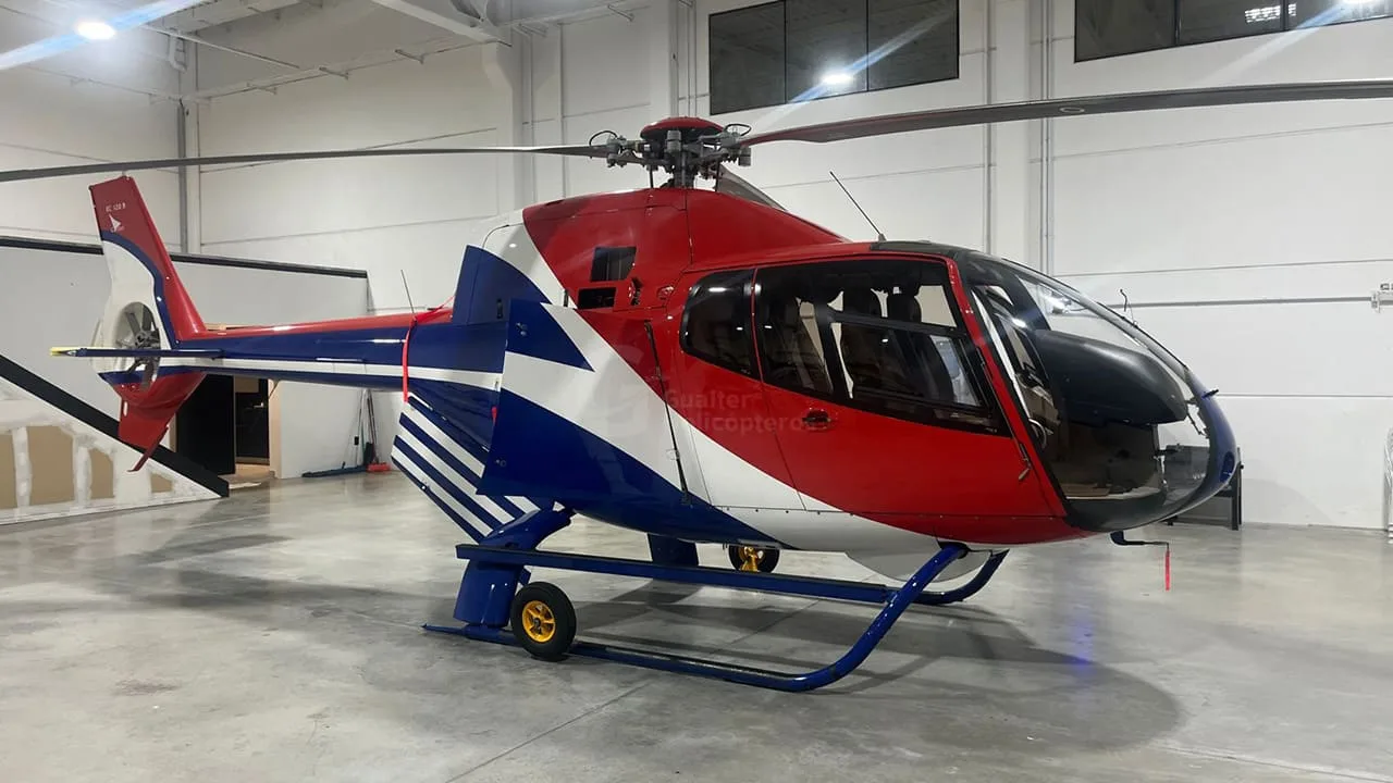 A red, white, and blue helicopter with a distinctive paint scheme sits in a well-lit hangar.