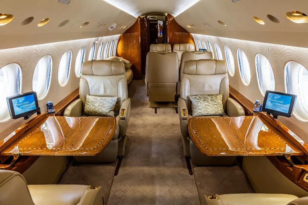 The private jet cabin with tan leather seats and polished wooden tables extended for use.