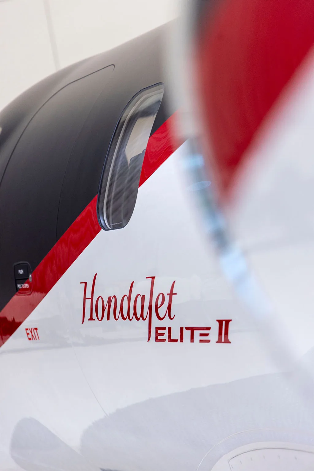A close-up view of the red 'HondaJet ELITE II' text and a window on the white fuselage of the aircraft, with a red and black stripe.
