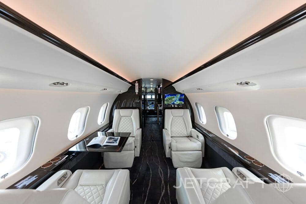 Forward view of the cabin of a Bombardier Global Express with white leather seats, a table, and a monitor.